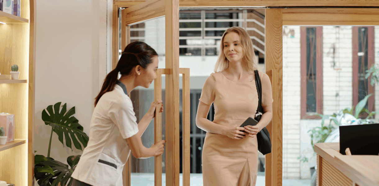 Esthéticienne accueillant une cliente à l’entrée d’un institut de beauté, illustrant la relation de confiance avant la vente en institut de beauté